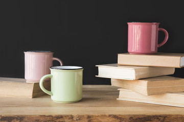 three colored cups and books on wooden table on black