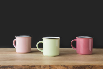 three colored cups on wooden table on black