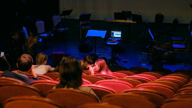 Back of conductor and musicians in concert hall and banister.