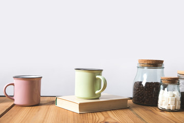 cups, book and glass bottles with coffee beans and refined sugar on table on white
