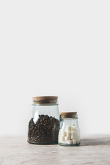 coffee beans and refined sugar in glass bottles on marble table on white