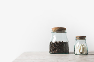 coffee beans and refined sugar in glass bottles on marble table on white