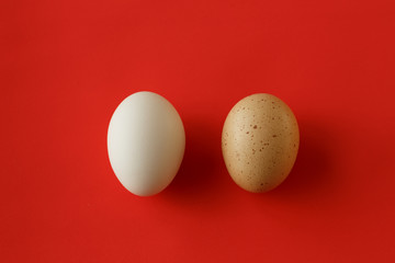 An egg with a yellow brown spot and a clean white egg on the red background - 189612406