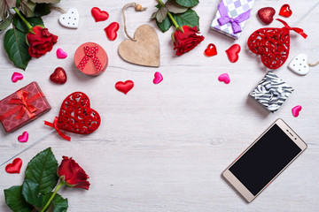 Wooden white background with hearts, gifts, red roses and smartphone. The concept of Valentine Day