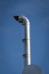 detail of a metal chimney illuminated by the sun in the background blue sky