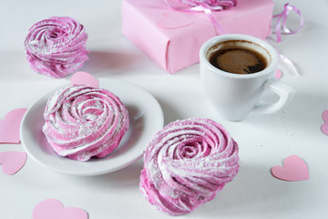 Gift in pink wrapping paper on a white background. Pink marshmallows and an espresso cup. Creative decor with paper hearts on the valentine's day. Wedding table. Holidays. Close up