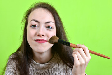 Beautiful young girl with cosmetic  make up brush on green background. Applying powder foundation on face skin.