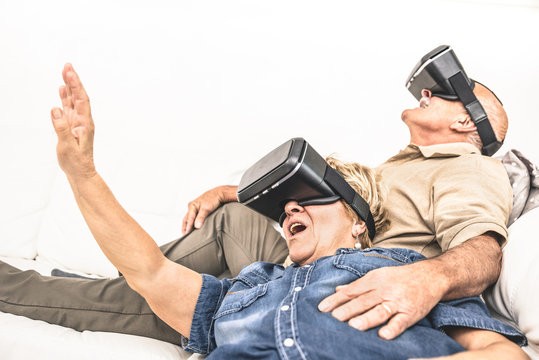 Senior mature couple having fun together with virtual reality headset sitting on sofa - Happy retired people using modern vr goggle glasses - New trends and technology concept and funny active elderly