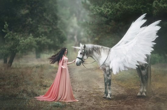 Beautiful, young elf, walking with a unicorn in the forest She is dressed in a long orange dress with a cloak. The plume beautifully waves in the wind. Artistic Photography
