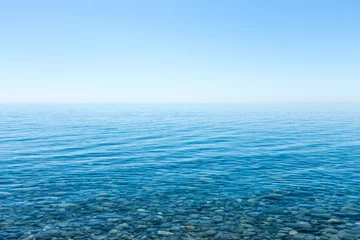 Photo sur Plexiglas Côte Beautiful seascape with a view of the horizon and a cloudless sky. Small smooth stones lying on the sea bottom with clear water on the shore