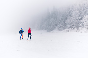 Two women trail running on snow in winter mountains