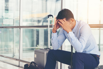 Serious businessman worrying something, sitting and touch his head at the airport terminal. Businessman miss his flight. Young man feeling sick before business trip.
