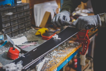 A male worker in a ski service workshop repairs the sliding surface of the skis. Close-up of a hand...