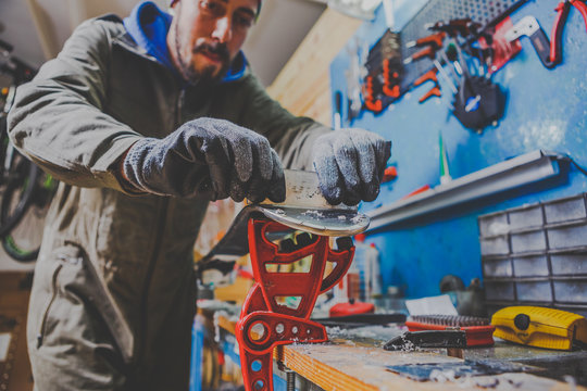 A male worker in a ski service workshop repairs the sliding surface of the skis. Close-up of a hand with a plastic scrapper for removing wax, removing new wax. Theme repair of ski curb