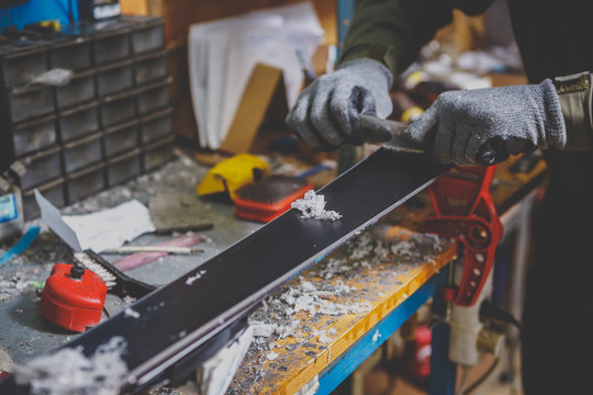 A male worker in a ski service workshop repairs the sliding surface of the skis. Close-up of a hand with a plastic scrapper for removing wax, removing new wax. Theme repair of ski curb