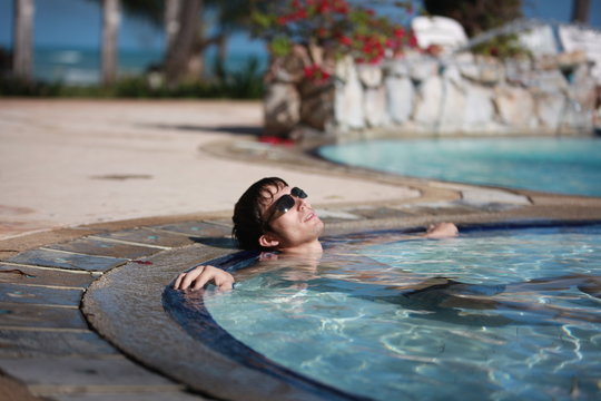Handsome young man in sunglasses lays in swimming pool resting. happiness, summer travel vacations hotel.