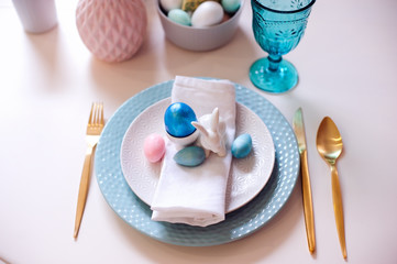 easter and spring festive table decorated in pink and blue colours with modern golden metalic cutlery, eggs and bunny.