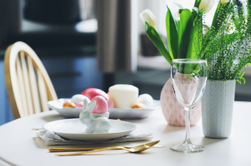 easter festive table details. Dining place decorated in trendy scandinavian style, pink and gold tones, with flowers, candles, bunny and eggs.