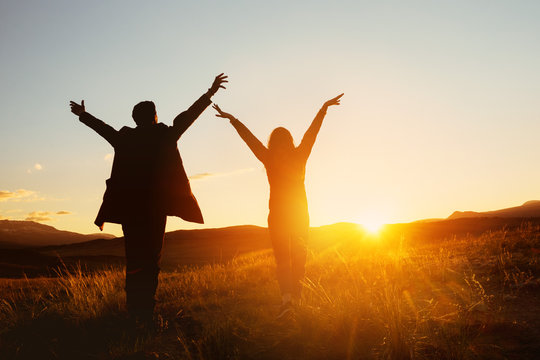Happy couple with raised hands against sunset