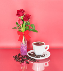 A cup of coffee, red roses in a bottle and scattered coffee beans