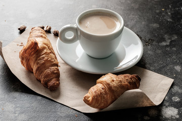 Morning espresso in a cup on a table with croissants in the front.