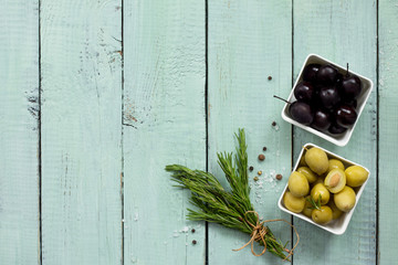 Wooden background with  black olives, green olives, olive oil, fresh rosemary and spices. Flat lay. Top view with copy space.