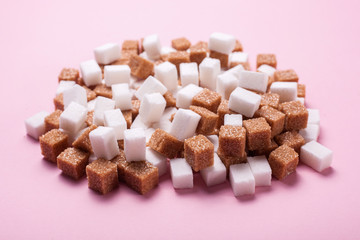 White and brown cane sugar cubes pile on a pink background.