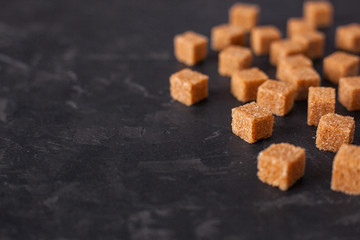 Brown cane sugar cubes pile on a black background. Copy space for text