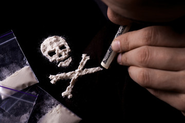 Drug dependence Kills. Junkie man sniffing a line of cocaine in the shape of a skull through a...
