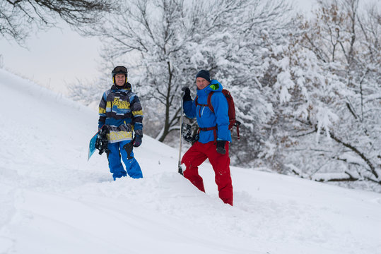 Two happy snowboarders are standing in the forest