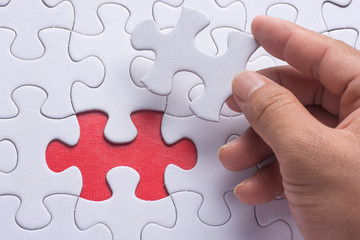 Fototapeta premium Hand holding piece of blank jigsaw puzzle with red background.