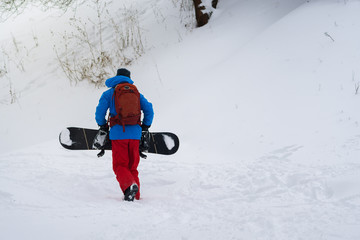 Snowboarder with backpack climbs up the slope