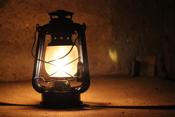 Kerosene lamp lights in a dark near a stone wall.