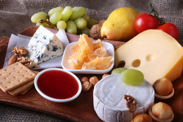 Assortment of cheese with fruits, grapes and nuts on a wooden serving tray.