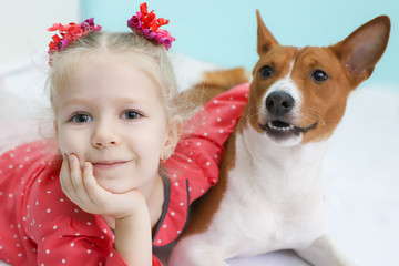 Little blonde curly girl hugging a basenji dog.