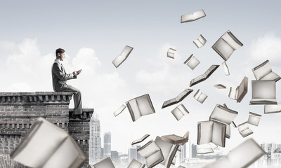 Man using smartphone and many books flying in air