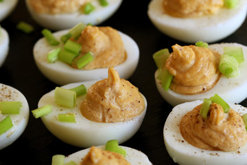Deviled eggs with cod livers with leek on on black background