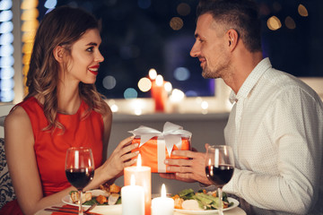 Young handsome man giving present to his girlfriend while have romantic dinner