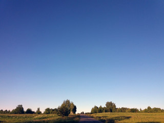 Background view of clear blue sky, meadow and a road at a low bottom. Sunny day, evening.