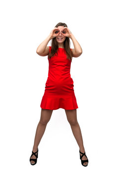 Girl in red dress in stockings and in high heels shoes is looking for something and she is holding her hands in front of her face like a binoculars isolated on white background.
