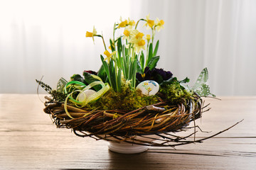 Easter table centerpiece decoration with daffodils and easter eggs arranged in a rustic wreath made of tree twigs