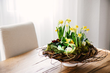 Easter table centerpiece decoration with daffodils and easter eggs arranged in a rustic wreath made of tree twigs
