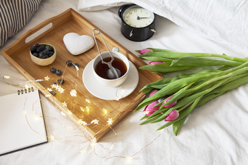 tray with tea and gingerbread in the shape of heart and a bouquet of tulips on the bed