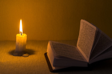 Education concept. Close-up view of old burning candle with shabby old book on table background. Focus on the candle