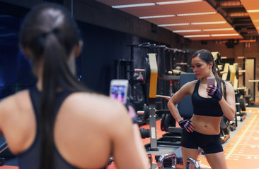 Fototapeta na wymiar woman with smartphone taking mirror selfie in gym