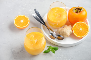 Fresh healthy smoothie with persimmon, orange and ginger on gray concrete background. Selective focus.