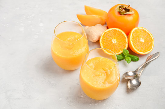 Fresh healthy smoothie with persimmon, orange and ginger on gray concrete background. Selective focus, copy space.