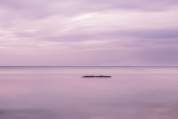 Obraz premium Sea open space and rocks in the water. Long exposure. Artistic photo, minimalism, simplicity and gentle lilac tones. 