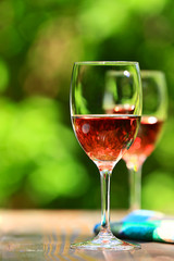 Two glasses of Shinning Rose Wine on wooden table with tablecloth, defocused bright and fresh green outdoors background 1