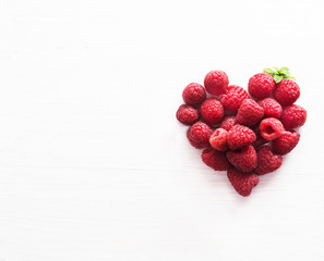 Raspberries in heart shape for valentine's or mothers day on white wooden background.